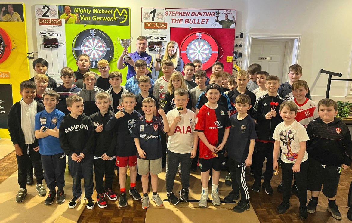 St Helens Darts Academy players surrounding champions Luke Littler and Eleanor Cairns.
